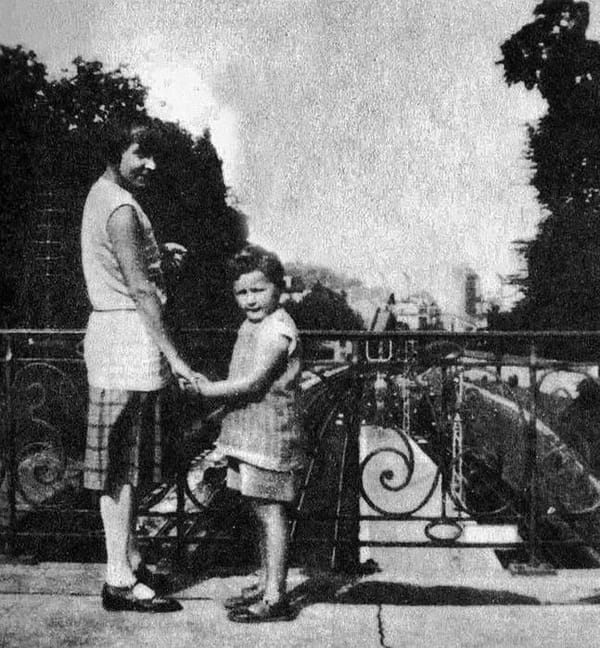 Чёрно-белая фотография: женщина и маленькая девочка держатся за руки у кованой ограды на фоне деревьев.