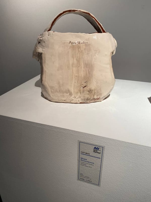 Глазурованная керамическая сумка с надписью Acne Studios на белом постаменте. Рядом табличка: лот № 42, Маша Колосовская, 2021, глина, глазурь.